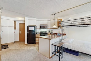 A compact kitchen with a refrigerator, microwave, and stove, a small island with a sink, and a bunk bed with a desk. - Cozy ski-in/out condo with shared hot tub and pool, mountain views (Winter Park)