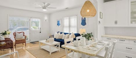 Un salón amplio con un sofá azul, muebles blancos, una mesa de comedor y una cocina con armarios blancos.