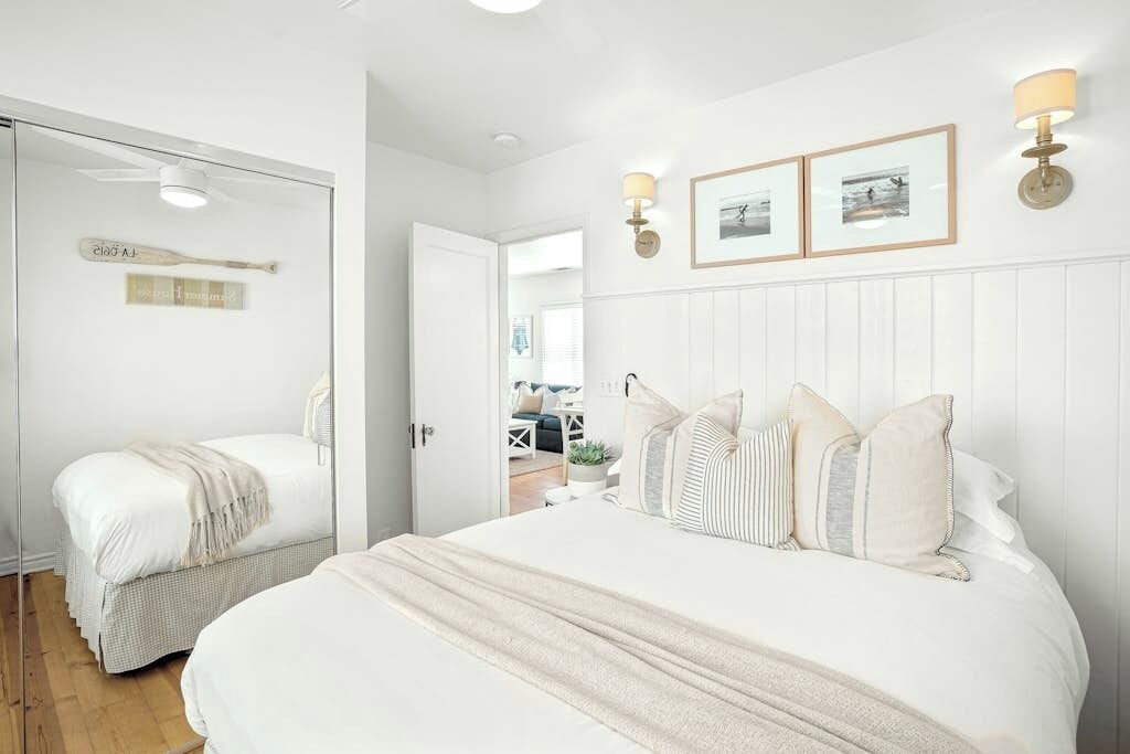 A bedroom with two beds, a white wall with framed pictures, and a door leading to another room.