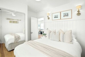 Ein Schlafzimmer mit zwei Betten, einer weißen Wand mit gerahmten Bildern und einer Tür zu einem anderen Raum.