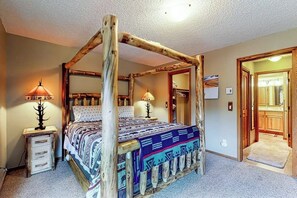Ein Himmelbett mit gemustertem Überwurf, einem Holz-Kopfteil und zwei Nachttischlampen.