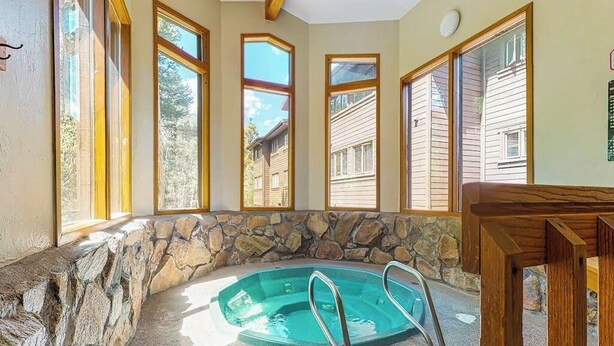 A stone-walled hot tub with metal ladders, large windows, and a view of neighboring houses. - Beautiful and Secluded Mountain Home w/ Access to Shared Amenities (Breckenridge)