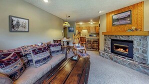 A living room with a sofa, a coffee table, a fireplace, and a kitchen in the background. - Beautiful and Secluded Mountain Home w/ Access to Shared Amenities (Breckenridge)