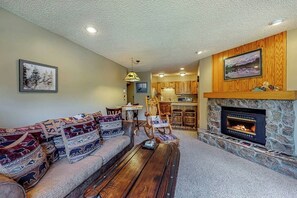 Ein Wohnzimmer mit einer Couch, einem Couchtisch, einem Kamin und einer Küche im Hintergrund.