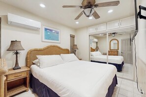 Ein Schlafzimmer mit zwei Betten, einem Deckenventilator, einer Klimaanlage und einem gerahmten Bild an der Wand.