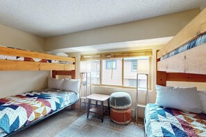 Ein Schlafsaalzimmer mit Etagenbetten, einem kleinen Schreibtisch, einem Stuhl und einem Fenster mit Jalousien.