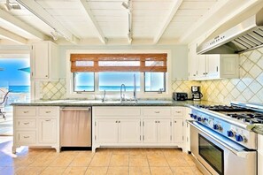 A kitchen with white cabinets, a large island, a stove, and a view of the ocean. - Duplex with breathtaking ocean views (Dana Point)