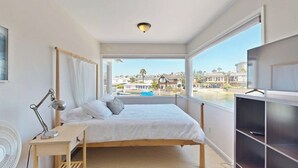Ein Schlafzimmer mit Bett, Nachttisch, Lampe und Blick auf die Stadt durch große Fenster.