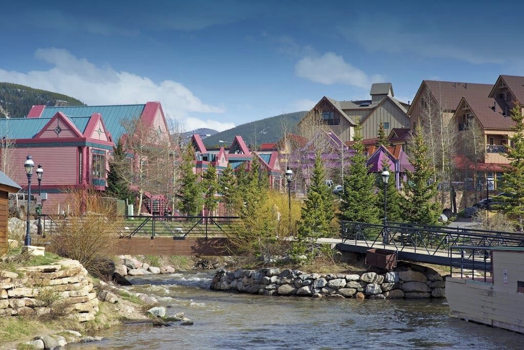 A riverside town with colorful buildings, a stone bridge, and a clear sky.