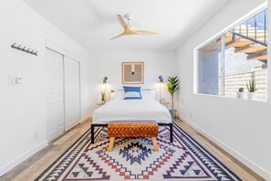 A bedroom with a bed, bedside tables, a ceiling fan, a window, and a patterned rug. - Charming gem near the beach with large backyard, cornhole, fast WiFi & grill (San Clemente)