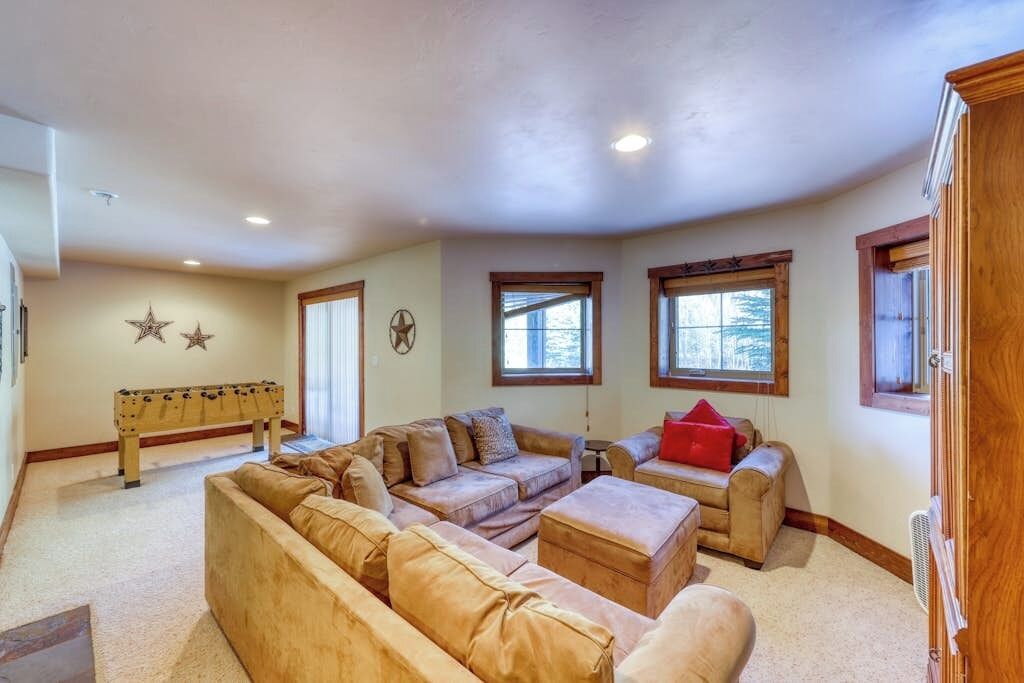 A spacious living room with a sectional sofa, ottomans, a foosball table, and large windows.