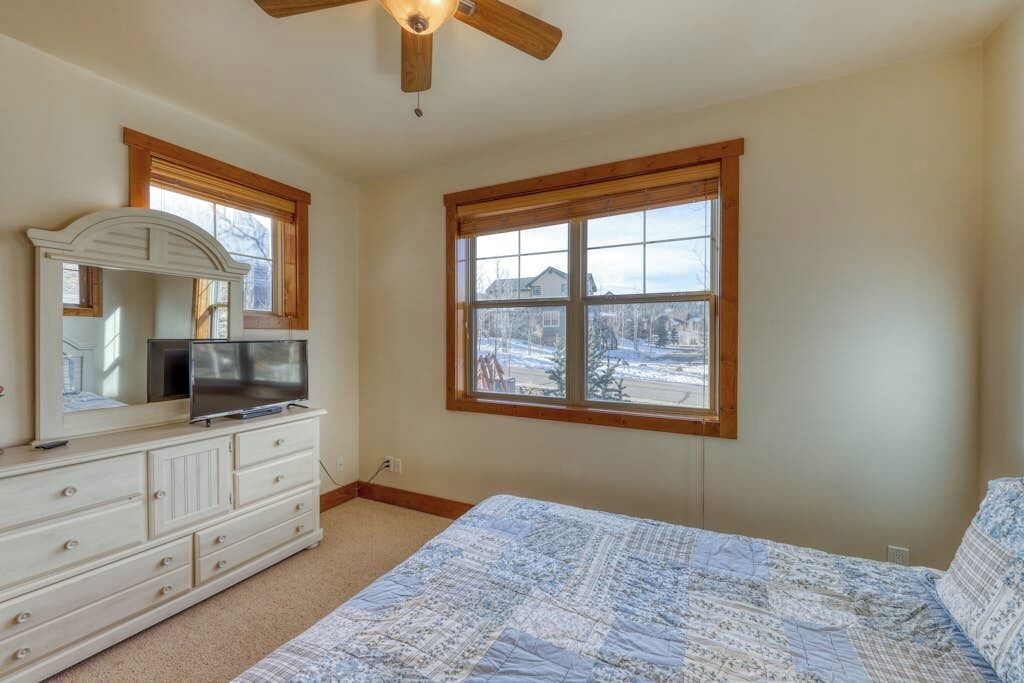 A bedroom with a bed, dresser, TV, and a large window with a view.