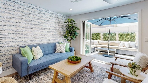 Un salon moderne avec un canapé bleu, une table basse en bois et une grande fenêtre donnant sur un patio.