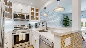 Une cuisine moderne avec des meubles blancs, des appareils en acier inoxydable, un mur d’accent en bois et des luminaires suspendus.