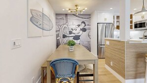 Une cuisine moderne dotée d’un réfrigérateur encastré, d’un coin repas avec une table et des chaises en bois, et d’une fresque murale.