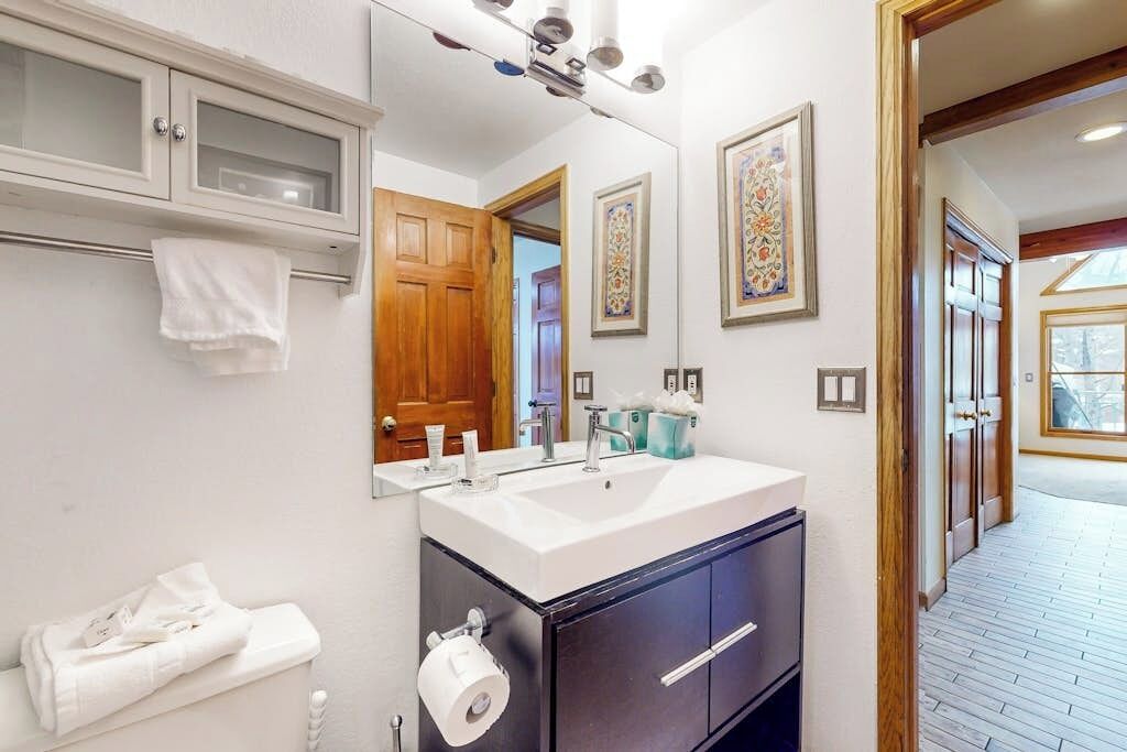 A bathroom with a white sink, a mirror, a towel rack, and a wooden door.