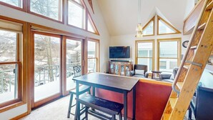 A high-ceiling room with large windows, a wooden table, a bench, and a television. - Dog-friendly condo right in the center of town - walk to & from skiing (Breckenridge)