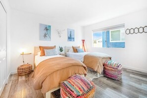 A bedroom with two beds, a window, and wall art.