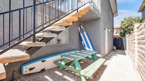 A residential outdoor area with a concrete staircase, a picnic table, and a blue and white surfboard leaning against a wall. - Convenient dog-friendly condo with free WiFi - right up from the beach (San Clemente)
