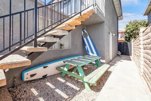 A residential outdoor area with a concrete staircase, a picnic table, and a blue and white surfboard leaning against a wall.