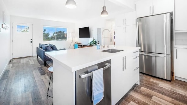 A modern kitchen with white cabinetry, a stainless steel refrigerator, and pendant lighting. - Convenient dog-friendly condo with free WiFi - right up from the beach (San Clemente)