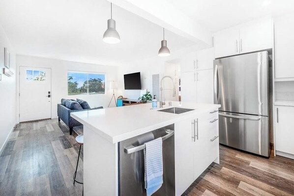 Una cocina moderna con armarios blancos, un refrigerador de acero inoxidable e iluminación colgante.