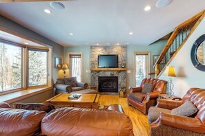 Ein gemütliches Wohnzimmer mit Ledersofas, einem Kamin, einem Fernseher und einer Treppe.