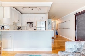 A modern kitchen with white cabinetry, a central island, and a dining area with a tufted sofa. - Glamorous, dog-friendly condo with pool, hot tub & W/D - snowbird-friendly (Newport Beach)