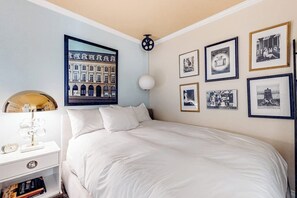 A bedroom with a large bed, a nightstand with a lamp, and a wall with framed pictures. - Glamorous, dog-friendly condo with pool, hot tub & W/D - snowbird-friendly (Newport Beach)