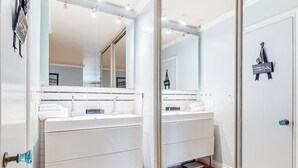 Une salle de bain moderne avec deux lavabos, un grand miroir et une porte ornée d’une plaque décorative.