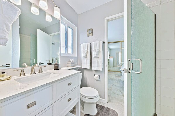 Une salle de bain avec un meuble-lavabo blanc, un grand miroir, des toilettes et un espace douche.