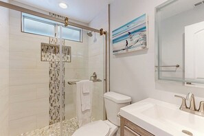 A modern bathroom with a glass shower enclosure, a toilet, and a sink with a mirror. - Redesigned all-suite retreat steps from beach with fireplace & AC (Newport Beach)