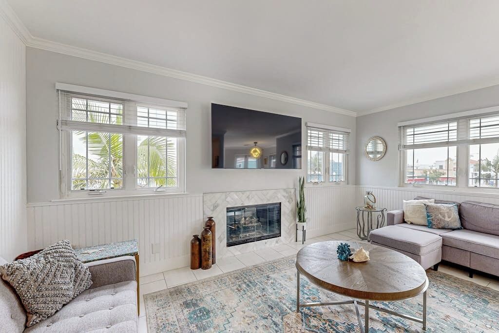 A living room with a fireplace, a sofa, a round coffee table, and large windows.