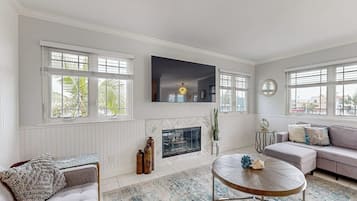 A living room with a fireplace, a sofa, a round coffee table, and large windows.