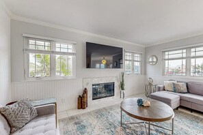 A living room with a fireplace, a sofa, a round coffee table, and large windows. - Redesigned all-suite retreat steps from beach with fireplace & AC (Newport Beach)