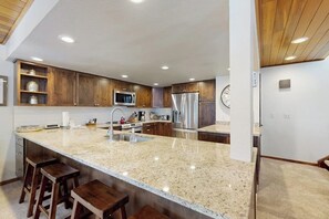 Eine Küche mit Granit-Arbeitsplatten, Holzschränken und Edelstahlgeräten, sowie einer Bar mit Barhocker.