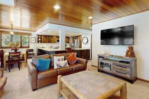 Ein modernes Wohnzimmer mit Holzboden, einem großen Flachbildfernseher, einem braunen Ledersofa und einem Essbereich mit Holzmöbeln.