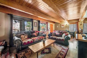 Ein gemütliches Wohnzimmer mit Holzbalkendecke, zwei Sofas mit gemusterten Kissen, einem Couchtisch und einem Teppich.