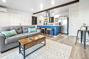 Ein Wohnzimmer mit einer Couch, einem Couchtisch und einer Küchenzeile inklusive Bar und Kühlschrank.