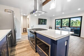 Eine moderne Küche mit Kochinsel, Edelstahlgeräten und einem großen Schiebeglastür zum Balkon.