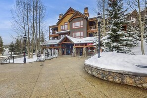 Una cabaña de varios pisos con fachada de piedra, balcones de madera y una entrada cubierta de nieve.