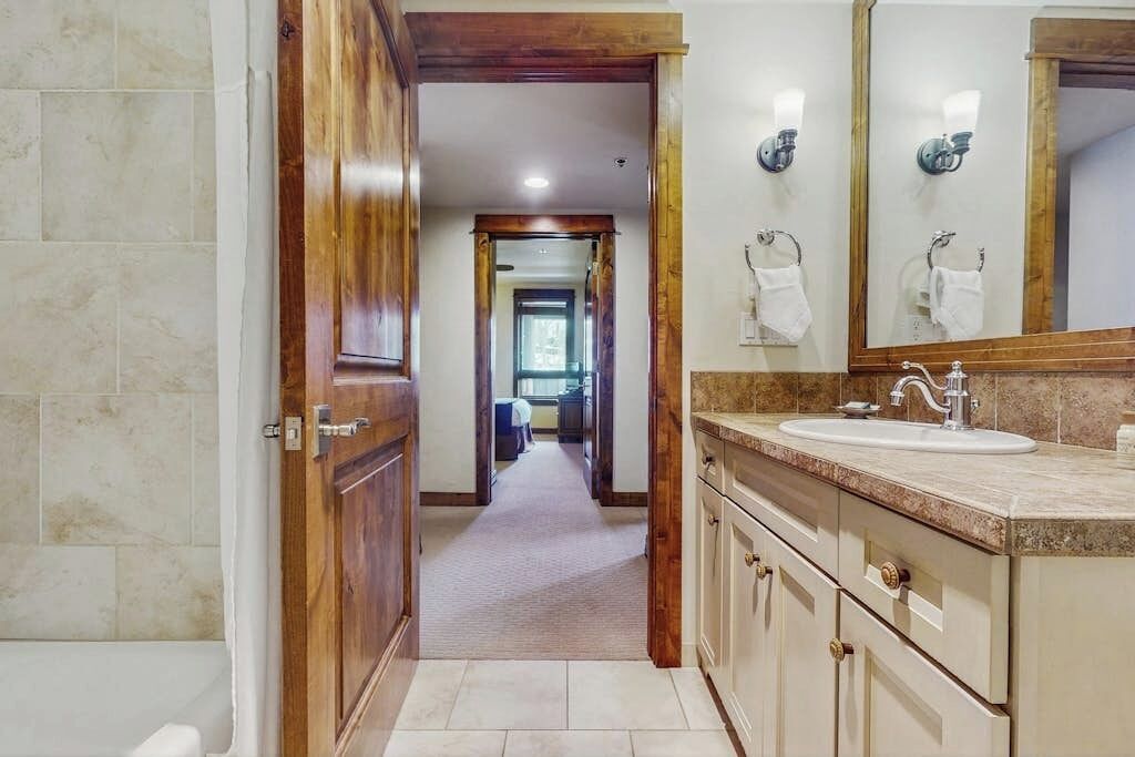 A bathroom with a wooden door, a sink with a mirror, and a towel rack.