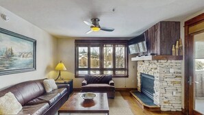 Una sala de estar con chimenea de piedra, sofá de cuero y televisor montado en la pared.
