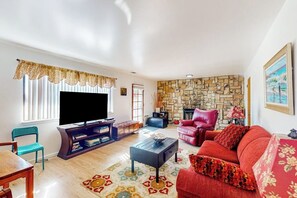 Een woonkamer met een televisie, rode bank, stenen muur en een open haard.