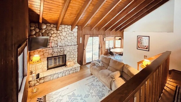 Una sala de estar acogedora con chimenea de piedra, vigas de madera, un sofá y un televisor montado en la pared.