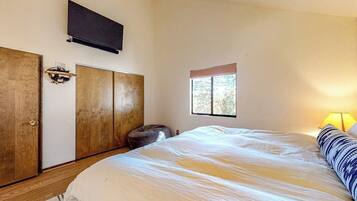 A bedroom with a bed, a television mounted on the wall, a window, and a lamp.