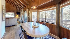 Un interior de madera con una mesa de comedor, sillas, un sofá y ventanas grandes.