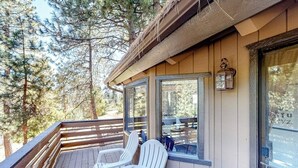 Una terraza de madera con sillas Adirondack, un farol y vistas a un bosque.