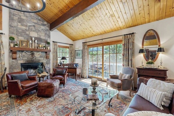 Una sala de estar acogedora con chimenea de piedra, sofás de cuero y un ventanal con cortinas.