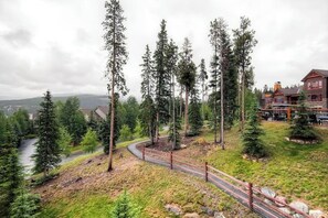 A mountainous landscape with a winding road, tall trees, and a lodge with a red facade. - Beautiful ski-in/ski-out villa with shared game room, hot tub, pool, & gym (Breckenridge)